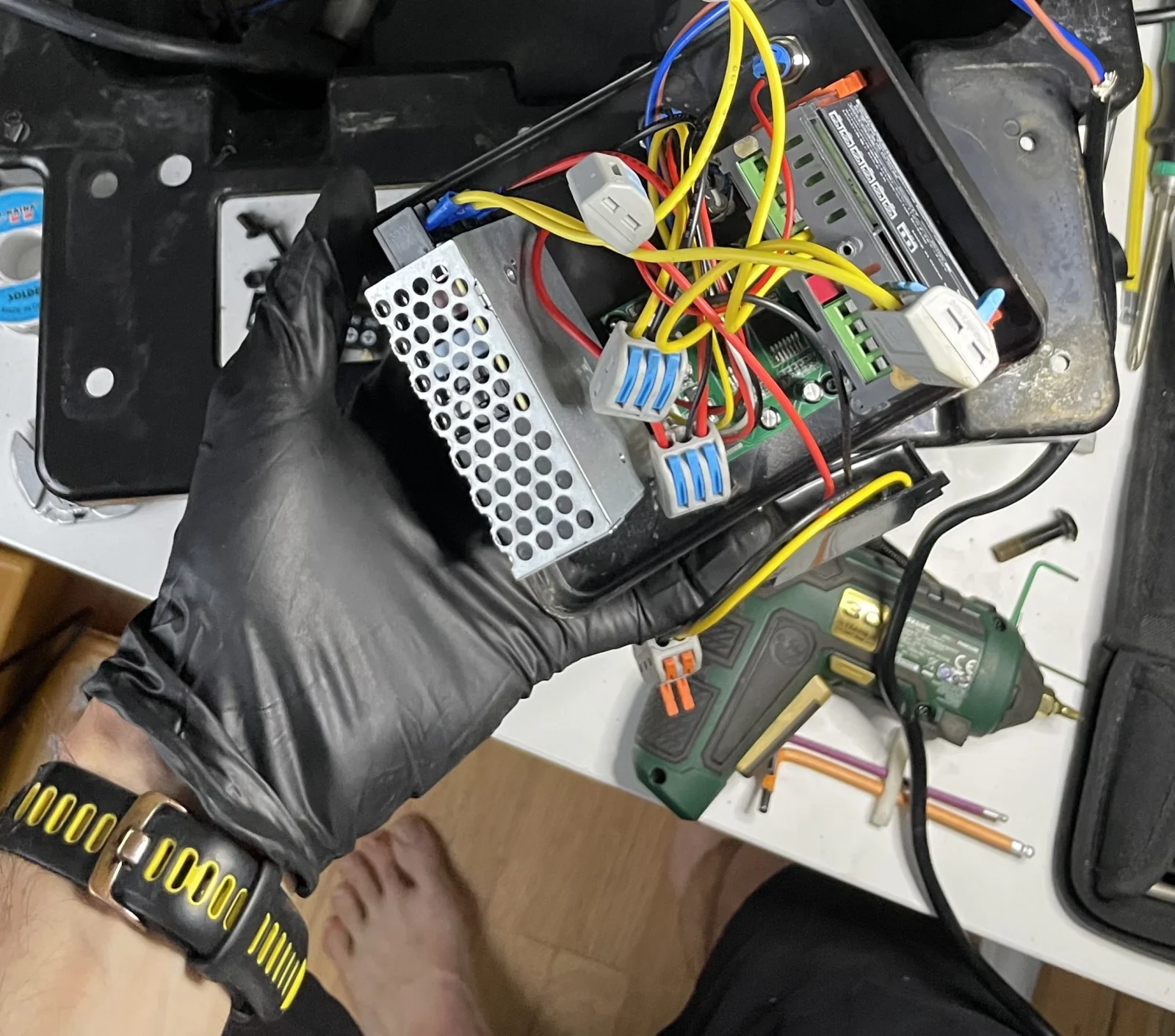 Hand holding the THD Darkroom CP Lift's removed control module, wires and connectors visible, next to the open bath enclosure